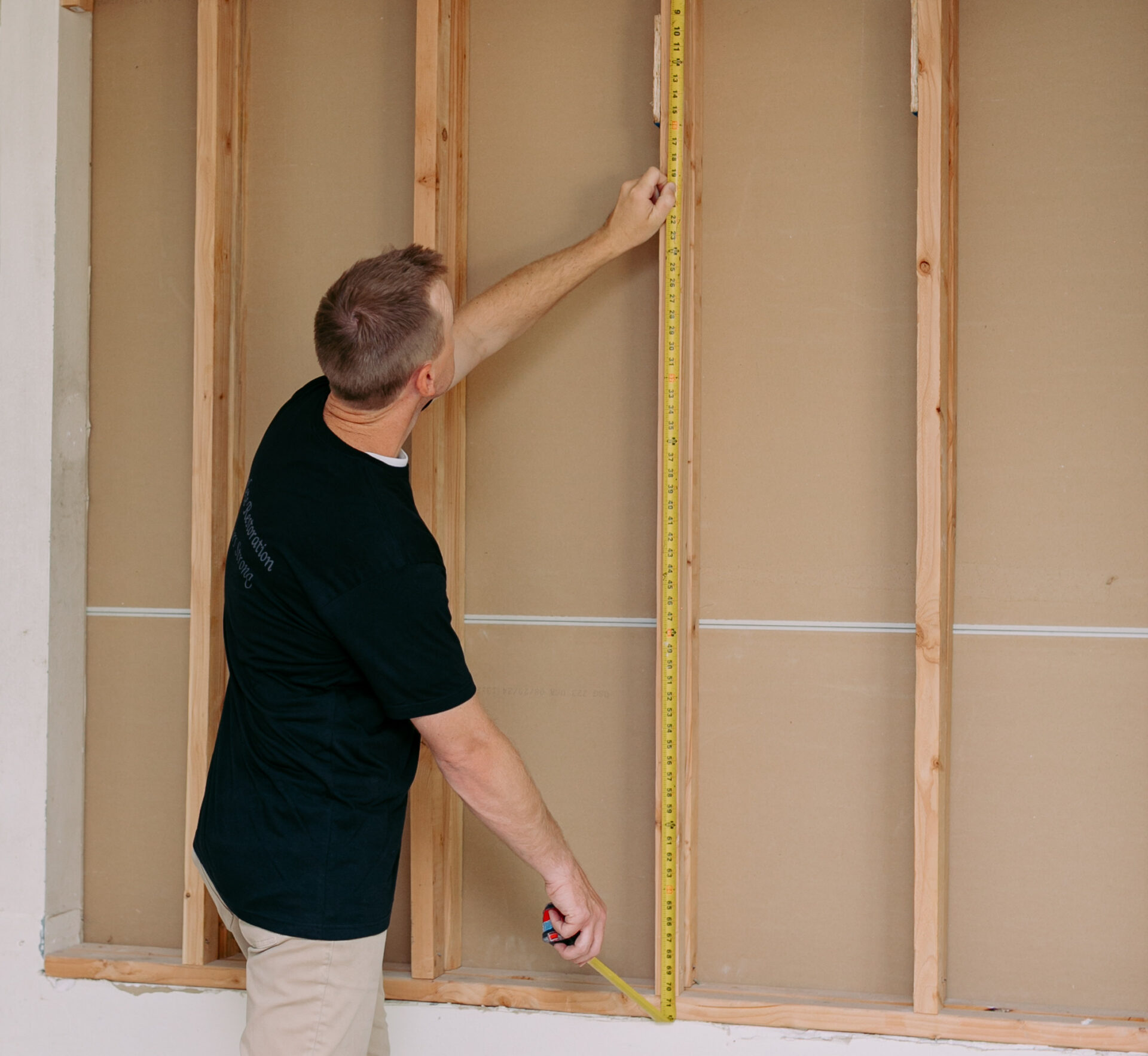 Reconstruction specialist measuring wall framing during full residential property rebuild